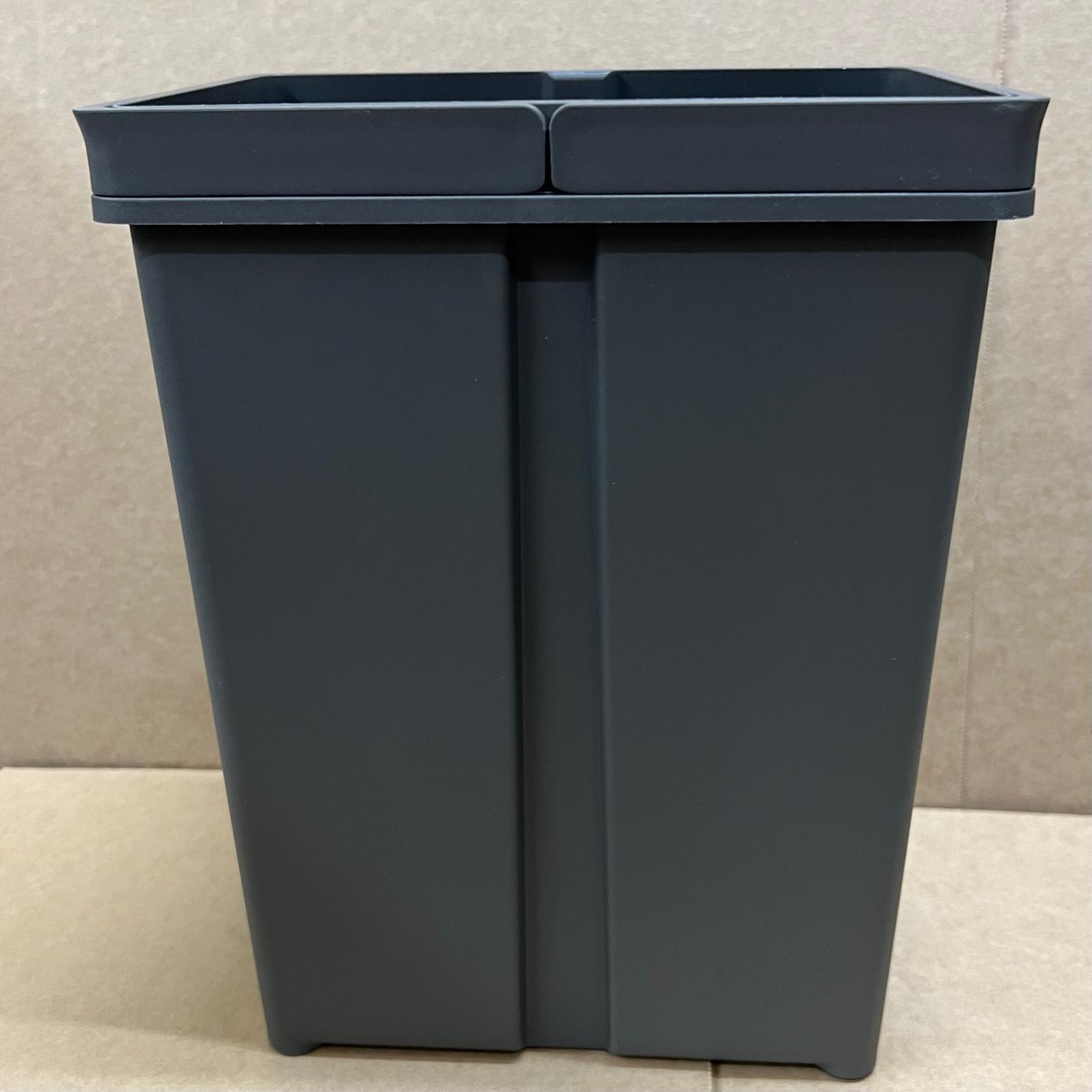 Dark gray recycling bin with two compartments on a beige floor.